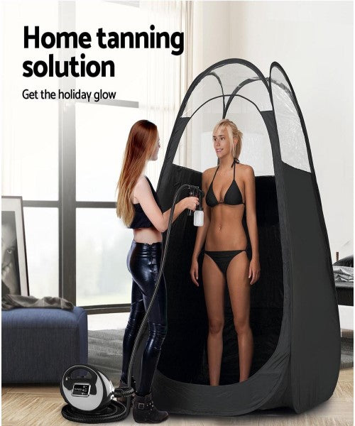 Pop up home or beach spray tan tent with a lady in a black bikini getting spray tan applied by a redhead lady wearing sexy black leather pants and top in a lounge room setting.