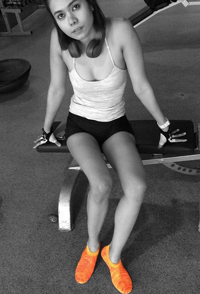 A very attractive lady sitting on a workout bench in gym setting wearing luminous bright orange Xtremekinetic bare foot minimal training shoe.