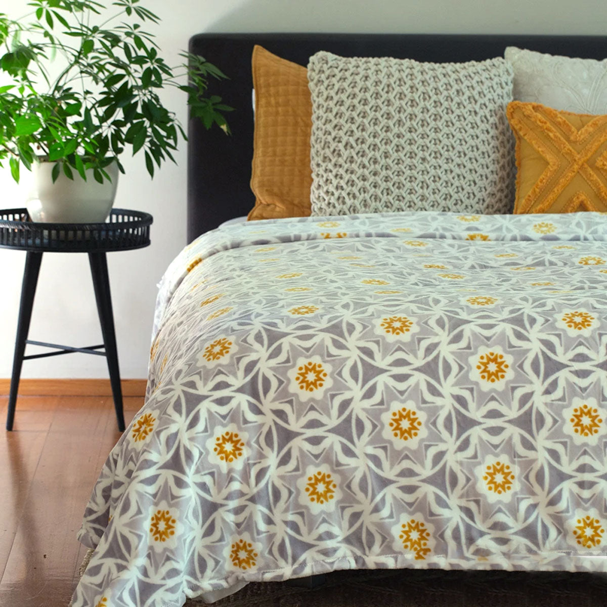 A sacred geometry style of circle and 5 interlinked eight pointed star design in grey and white with an orange center burst on a bed spread or doona on a bed with a little table in a bedroom setting.